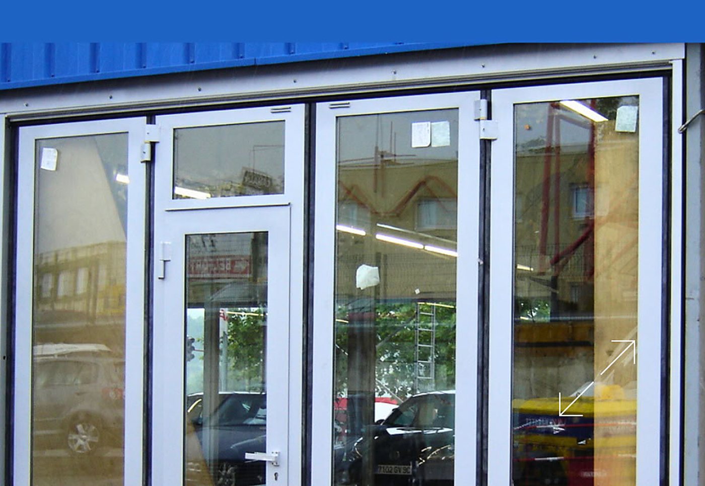 Façade d'un local à menuiseries blanches et grandes vitres, avec une porte vitrée et des reflets de voitures et d'immeubles.