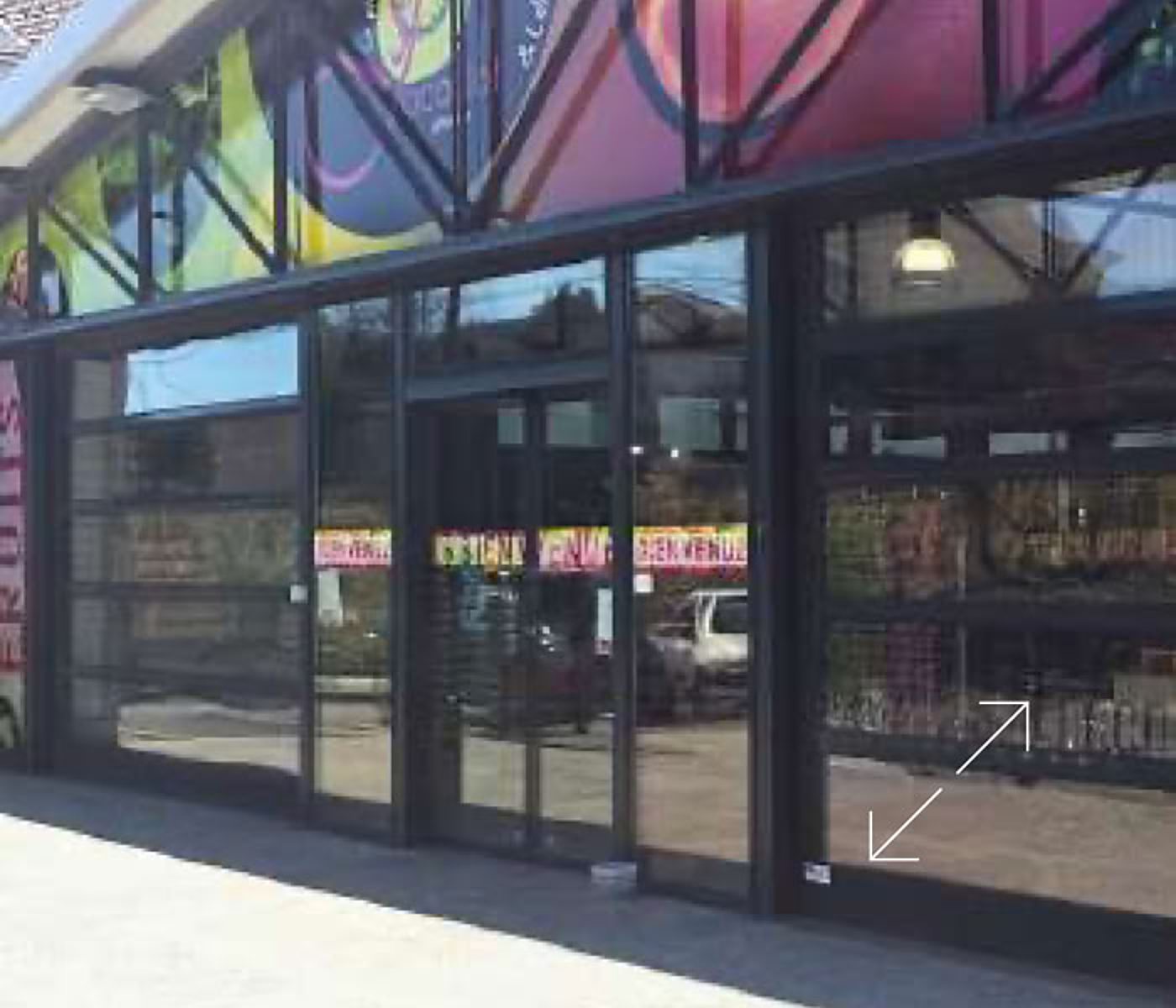 Façade vitrée d'un magasin avec une porte d'entrée et une grande fresque colorée en hauteur, sous un ciel dégagé.