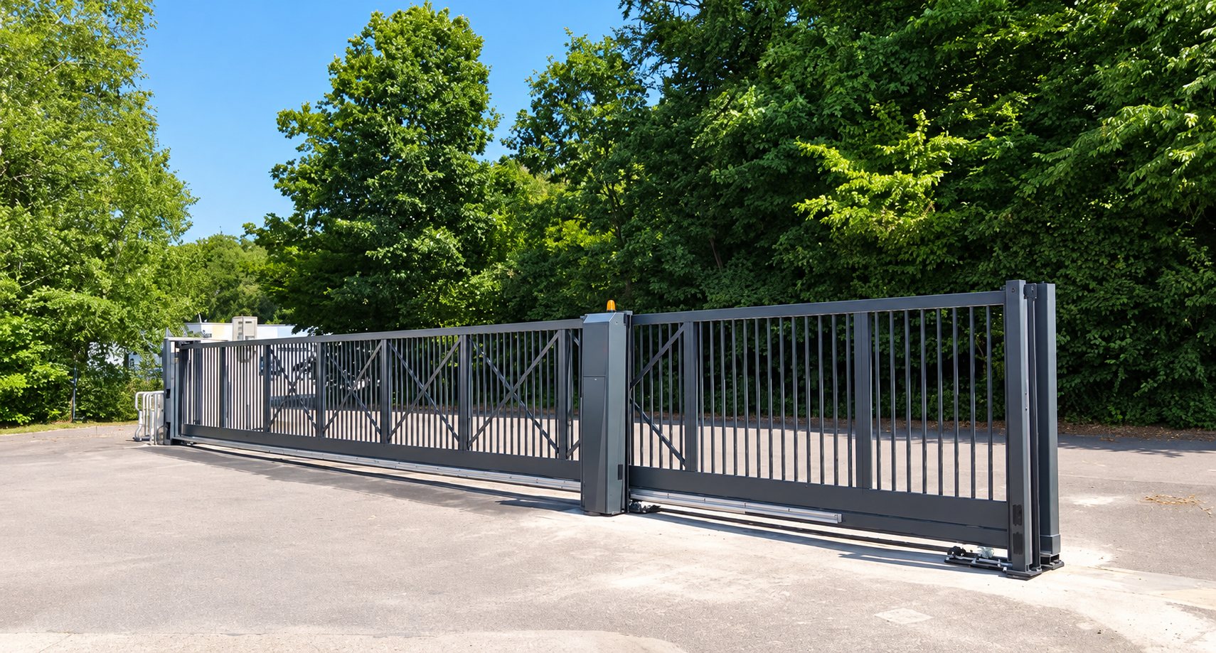 Un grand portail coulissant en métal gris anthracite à barreaux verticaux, installé à l'entrée d'un parking entouré d'arbres.