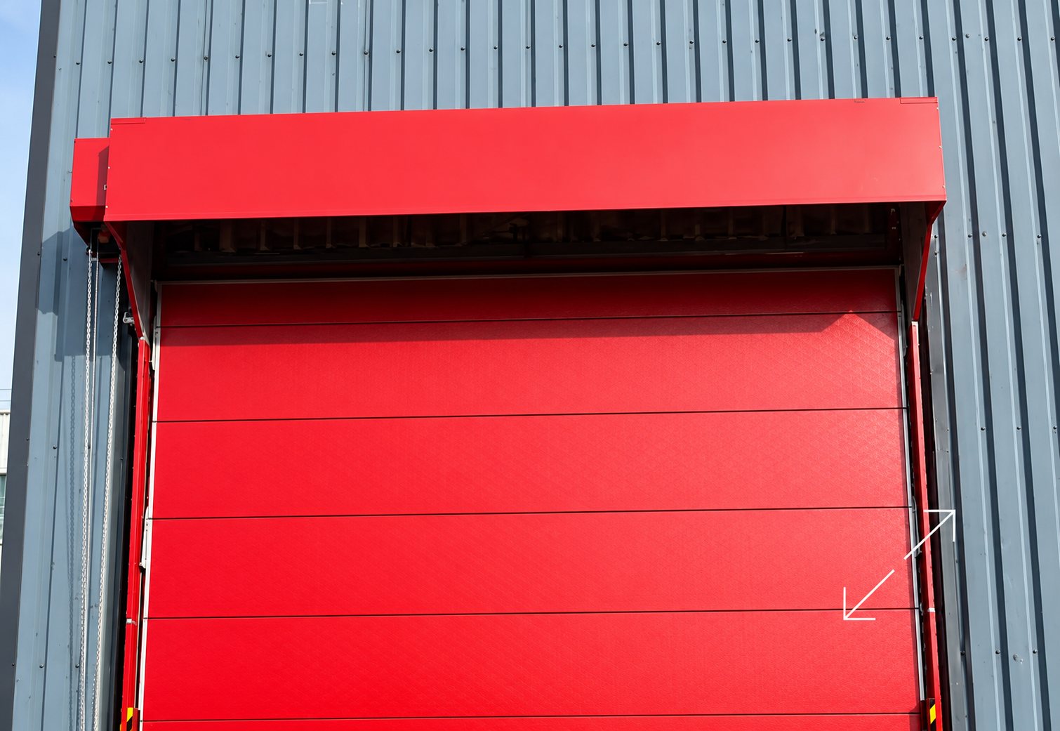 Une grande porte industrielle rouge avec son caisson est installée sur la façade d'un bâtiment en bardage métallique gris.