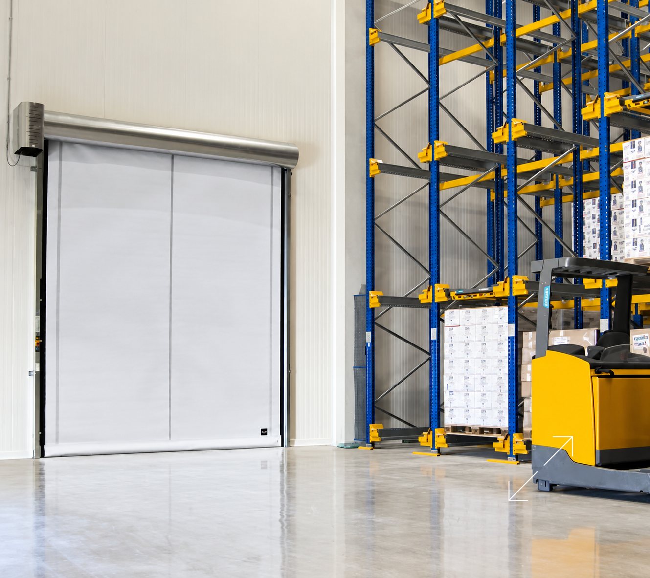 Une porte industrielle souple et rapide de couleur claire installée dans un entrepôt, à côté de hauts rayonnages bleus et jaunes et d'un chariot élévateur jaune.