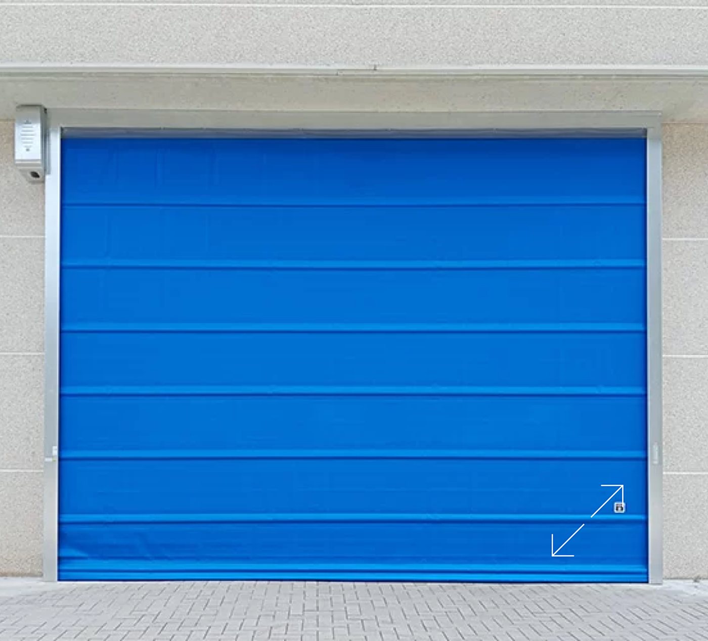 Une porte industrielle rapide à tablier souple bleu, encadrée de métal gris, est installée dans un mur beige au-dessus d'un sol pavé.